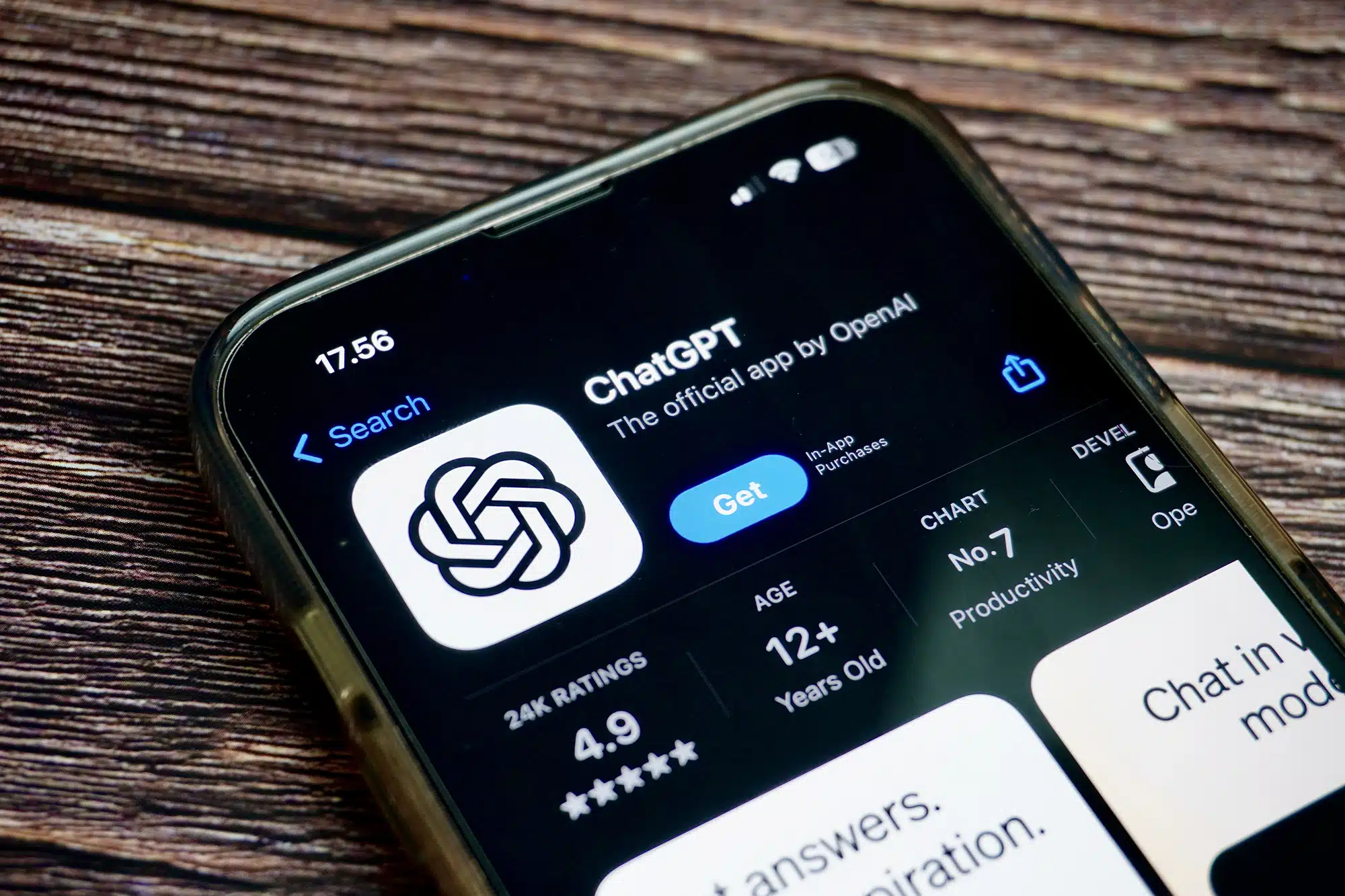 Экран смартфона с приложением ChatGPT от OpenAI в App Store рейтинг 4.9 звезды категория продуктивность значок в виде черно-белого узла фон деревянная поверхность