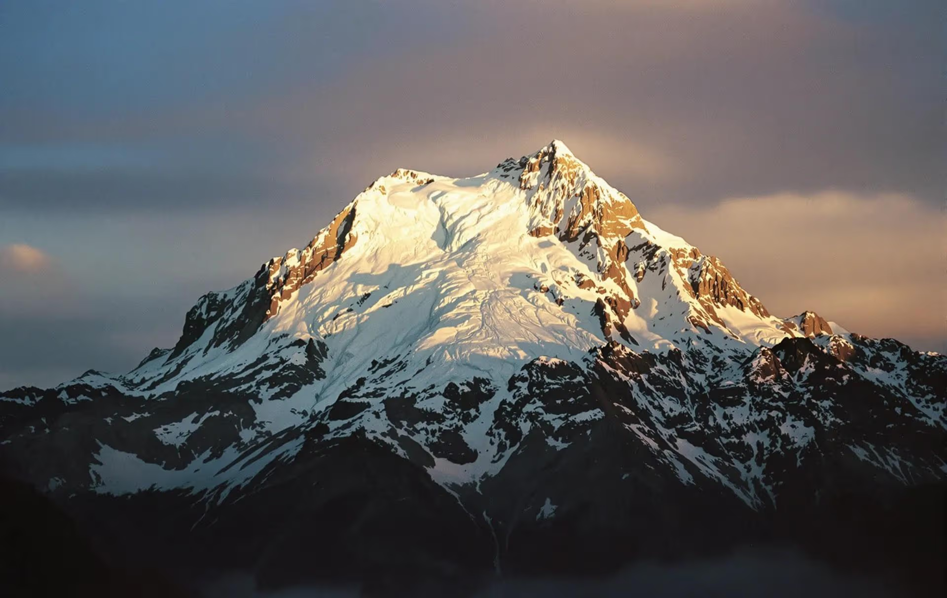 Заснеженная вершина горы освещенная солнечными лучами скалистый рельеф контраст света и тени природная красота рассвет или закат величие горного пейзажа